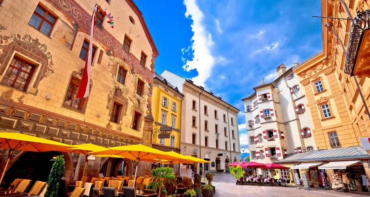 Place européenne charmante avec des bâtiments traditionnels et des parasols.