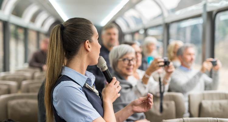À l'intérieur d'un wagon à toit de verre, un guide parle dans un microphone tandis que les passagers, prêts à photographier, se concentrent sur le paysage qui défile.