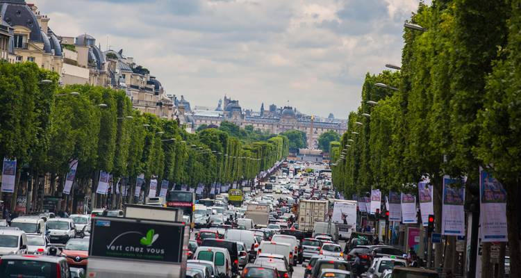 Avenida parisina muy transitada, llena de árboles, con mucho tráfico extendiéndose hacia el Arco de Triunfo