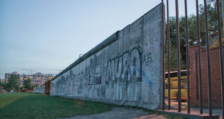 Segmento de hormigón del Muro de Berlín cubierto de grafitis extendiéndose hacia la distancia al atardecer.