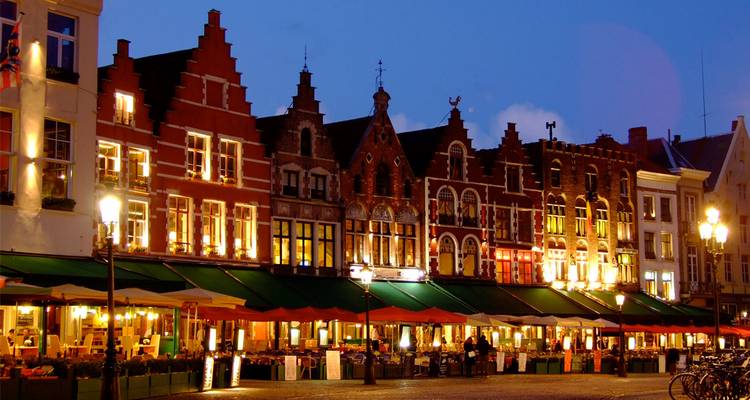 Los edificios de frontón escalonado iluminados de la Plaza del Mercado de Brujas brillan al atardecer con animadas terrazas de cafés abajo.