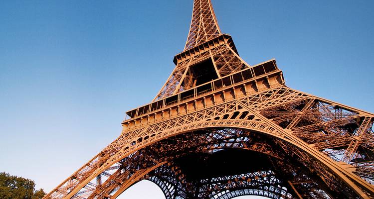Vista de ángulo bajo de la intrincada celosía de hierro de la Torre Eiffel contra un cielo azul despejado.