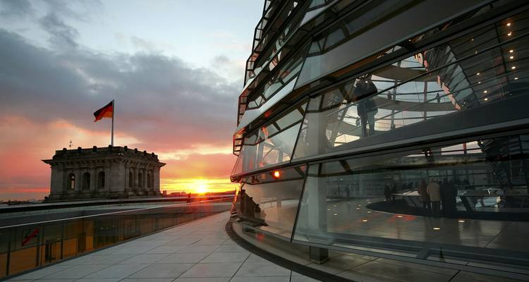 La cúpula de cristal del Reichstag de Berlín refleja la puesta de sol mientras la bandera alemana ondea sobre el histórico edificio del parlamento.