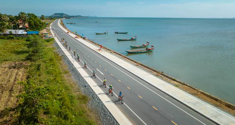 Des cyclistes roulant le long d'une route côtière avec des bateaux sur l'eau.