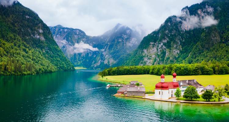 Lac pittoresque avec une église et des montagnes en arrière-plan.