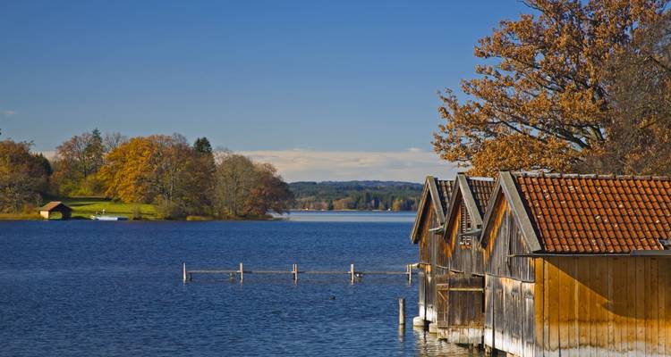Vue au bord du lac avec des hangars à bateaux en bois et des arbres d'automne.