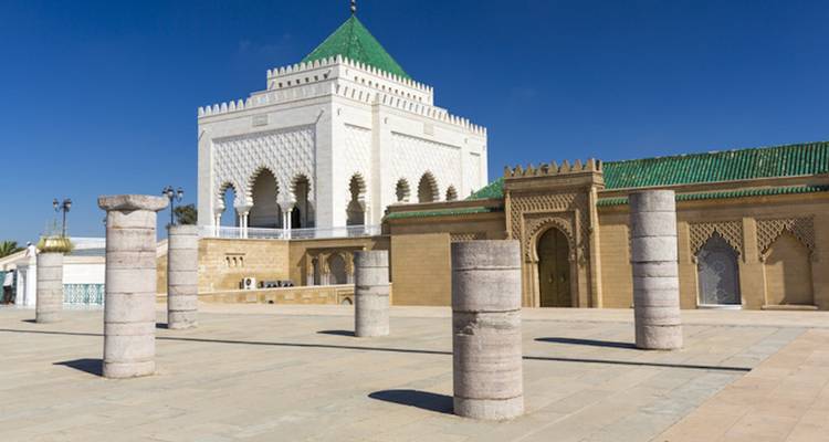 White mausoleum with green roof and historic pillars.