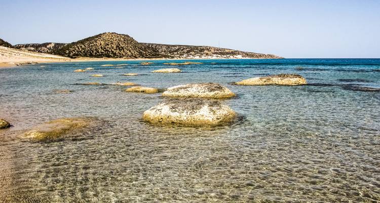 Clear water with rocks and distant hills under a blue sky.