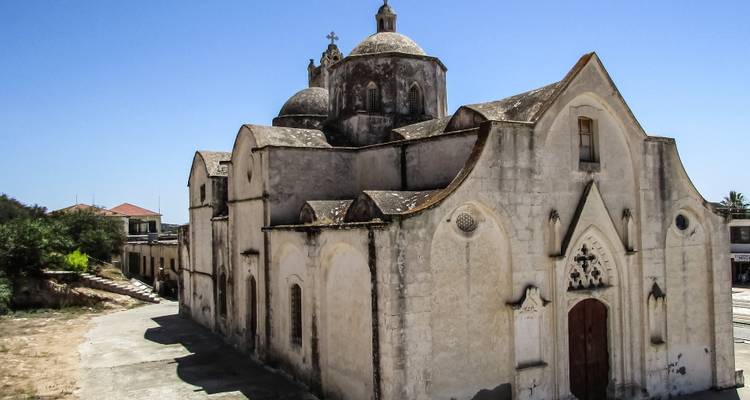 Old stone church with domes and pointed arches under a blue sky.