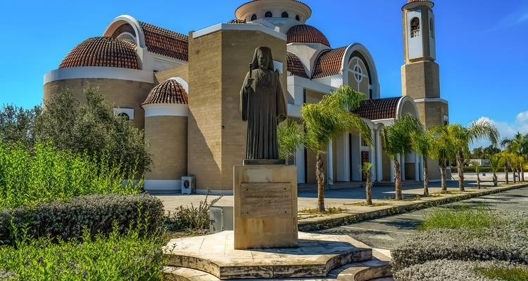 Statue in front of a modern church with palm trees.