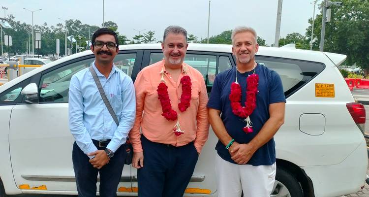Three men wearing welcome garlands posing in front of a white tourist vehicle