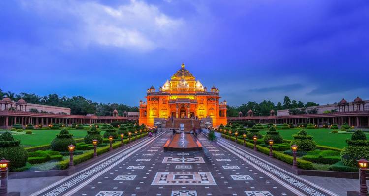 Akshardham Temple illuminated in golden light with manicured gardens under a dramatic twilight sky