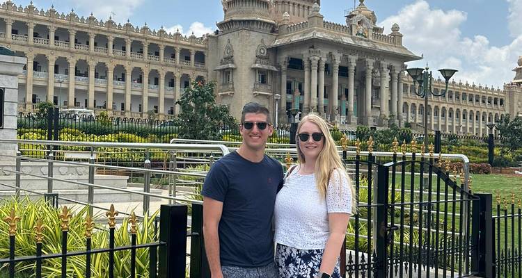 Couple debout devant un bâtiment iconique avec des colonnes et des jardins.