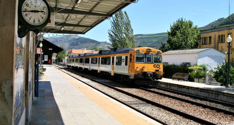 A train at a rural station with mountains in the backdrop.