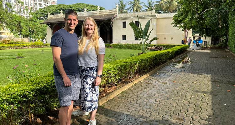 Couple posant dans un jardin avec un bâtiment historique en arrière-plan.