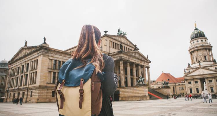 Una mujer con una mochila frente a edificios históricos en una plaza empedrada.