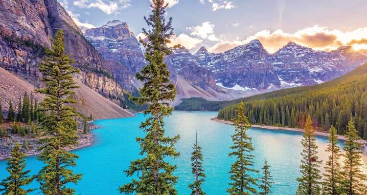 Stunning view over glacial-blue Moraine Lake framed by tall evergreens and the snow-dusted Valley of the Ten Peaks at sunset.