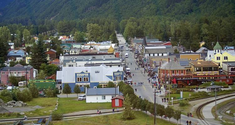 Busy main street of a small Alaskan town surrounded by green mountains and colourful wooden buildings.
