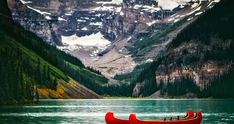 Two bright red canoes rest on a mirror-calm turquoise lake beneath towering glacier-clad mountains.