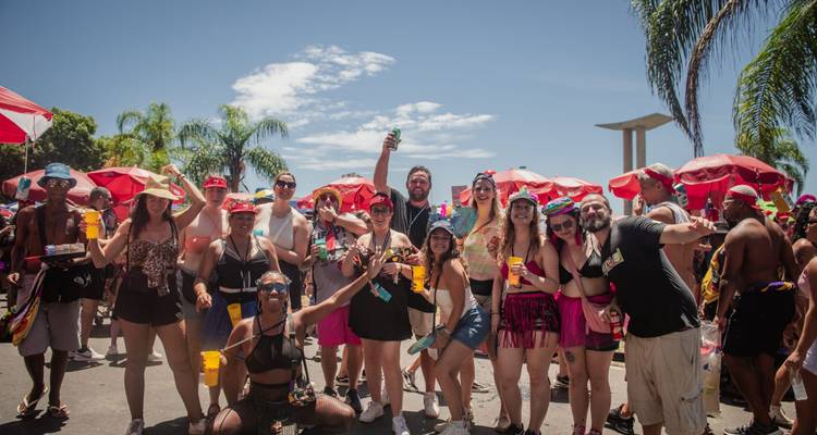 Grupo de personas con vestimenta colorida celebrando al aire libre bajo sombrillas rojas.