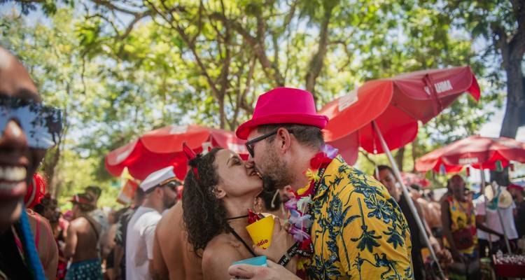 Pareja besándose al aire libre con vestimenta colorida y sombrillas rojas.