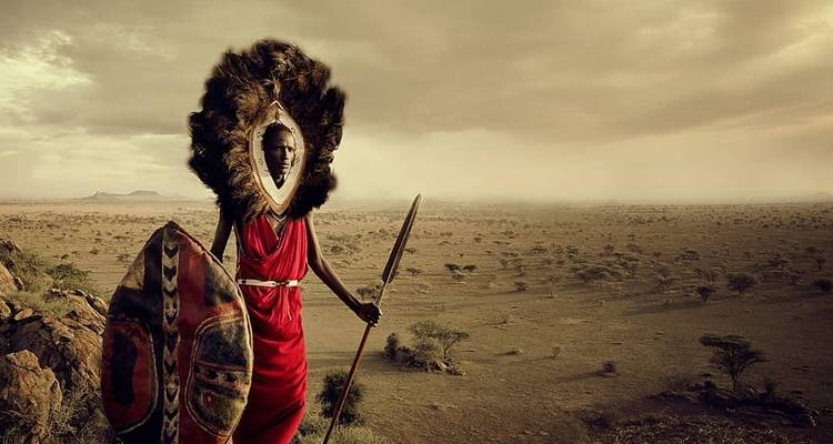 Traditional Maasai warrior with spear and shield standing in a vast landscape.