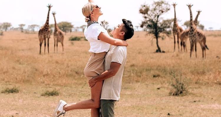 Couple posing with giraffes in the background on a savannah.