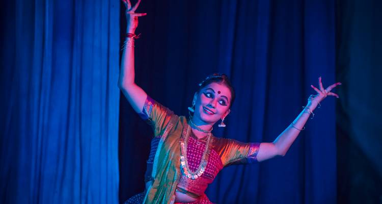 Klassieke Indiase danser die optreedt op het podium met dramatische belichting.