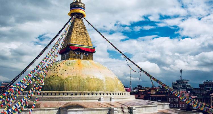 Large stupa with prayer flags and city view.