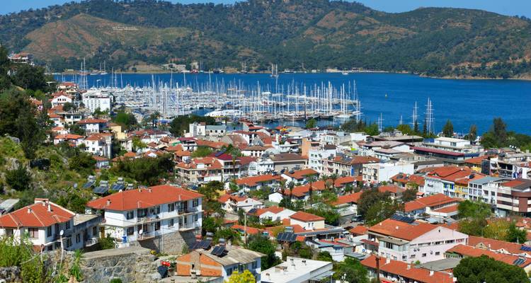 Pueblo de Fethiye con techos de tejas rojas con vista a un gran puerto deportivo de yates y bahía azul.