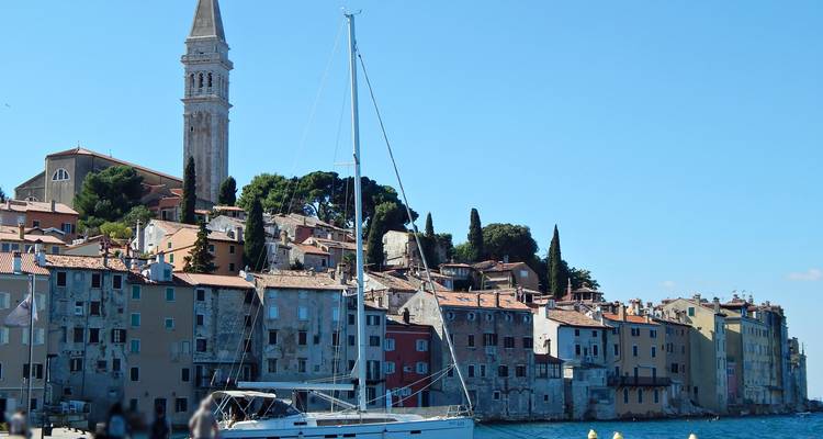 Horizonte junto al mar de Rovinj con un velero en primer plano y una torre de iglesia elevándose sobre los tejados de terracota.