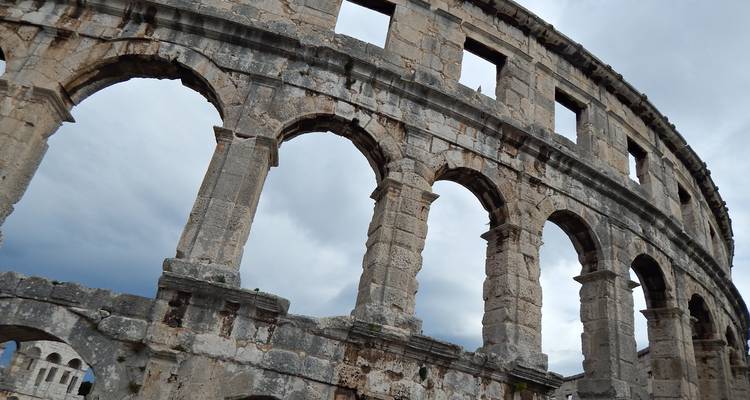 Nahaufnahme aus spitzem Winkel der massiven Steinbögen des römischen Amphitheaters von Pula vor einem düsteren Himmel.