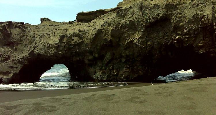 Küstenfelsformation mit Bögen über einem Sandstrand.
