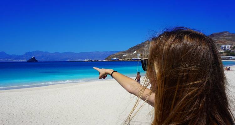 Person, die auf das Meer zeigt an einem wunderschönen Strand mit Bergen im Hintergrund.