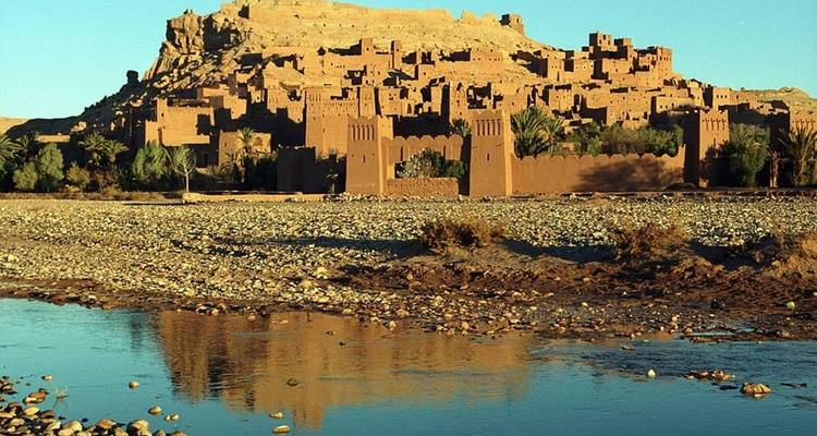 Reflection of an ancient fortress against a river with a clear blue sky.