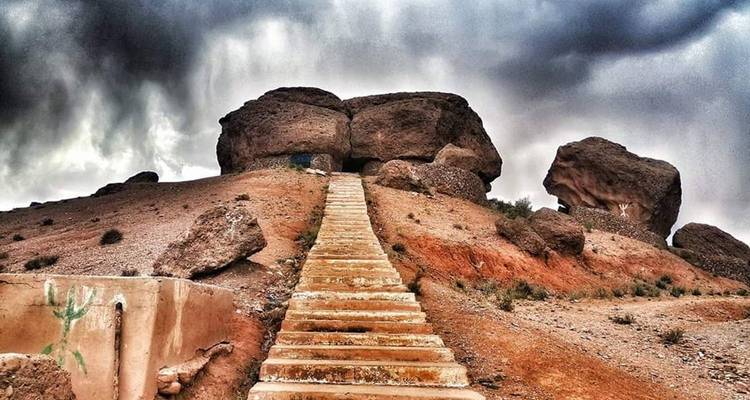 Escalones que conducen hacia grandes formaciones rocosas bajo un cielo dramático.