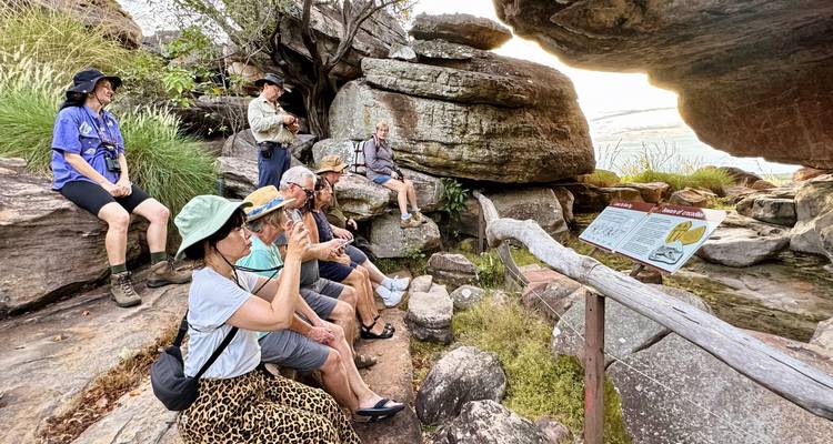 Groupe de touristes assis sur un rebord rocheux apprenant la culture indigène dans un abri sous roche au coucher du soleil