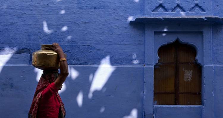 Een vrouw die een pot op haar hoofd draagt voor een blauwe muur.