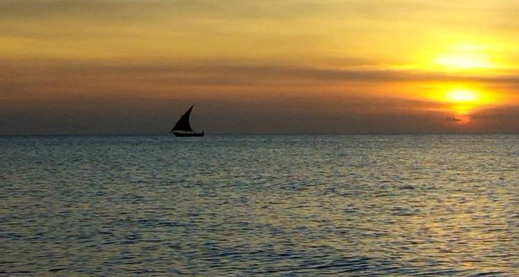 Silhouetted sailboat on the ocean during sunset.