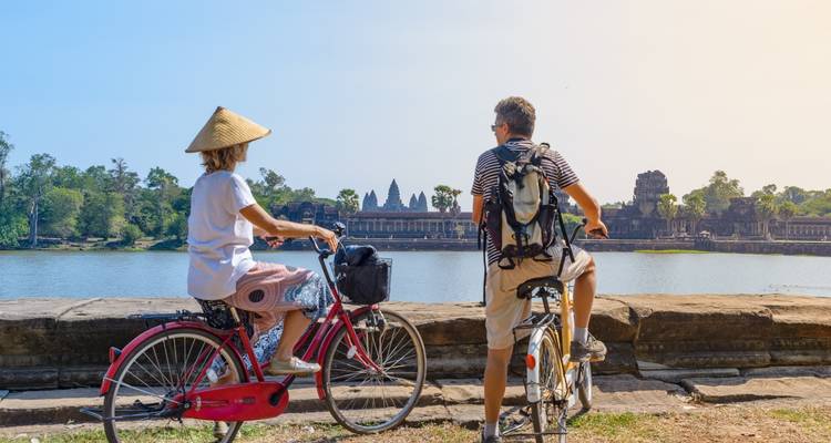 Twee mensen op fietsen die uitkijken over een meer met een tempel op de achtergrond.