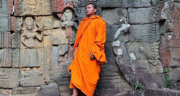 Mönch in orangefarbenem Gewand steht neben alter Tempelmauer.