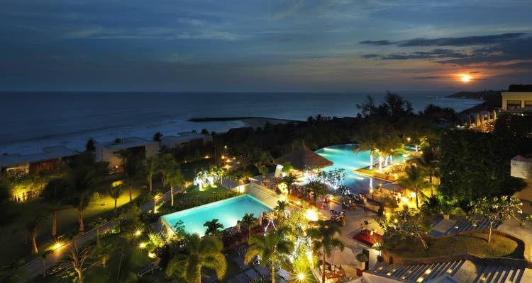 Nachtansicht eines Resorts mit Pools und Beleuchtung in der Nähe einer Küstenlinie.