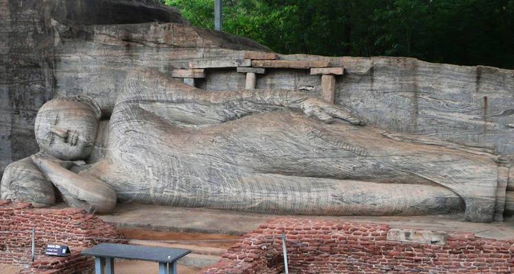 Statue de Bouddha couché sculptée dans la roche avec des ruines environnantes.