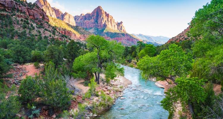 Un río que fluye a través de un valle verde y exuberante con imponentes formaciones de roca roja.