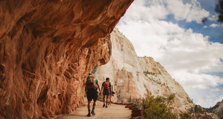 Los mochileros caminan por un sendero pegado al acantilado bajo enormes muros de arenisca roja en el Parque Nacional Zion.