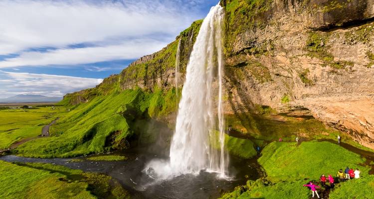 Gran cascada cayendo por un acantilado verde hacia una piscina natural con personas cerca.
