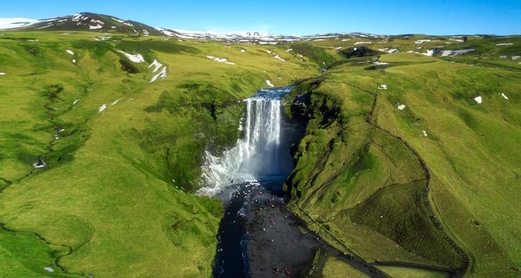 Vista aérea panorámica de una gran cascada en un valle verde con personas visibles.