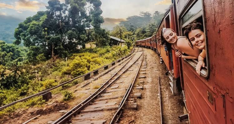 Deux femmes penchées à la fenêtre d'un train dans un paysage verdoyant luxuriant.