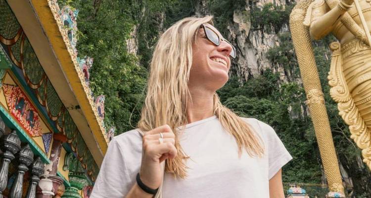 Glimlachende vrouw met zonnebril die de kleurrijke trappen en kalksteen rotsen van Batu Caves bewondert