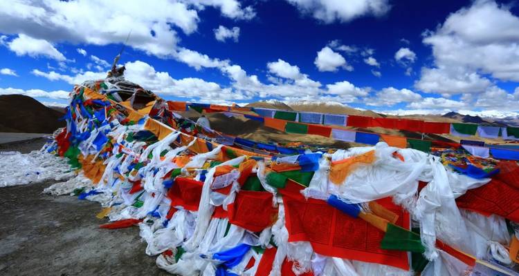 Banderas de oración coloridas contra un paisaje montañoso y cielo azul.
